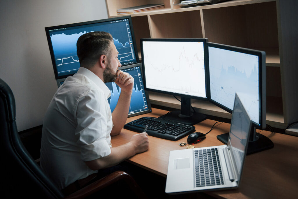 modern office worker bearded man white shirt sitting room with multiple computer screens index charts scaled